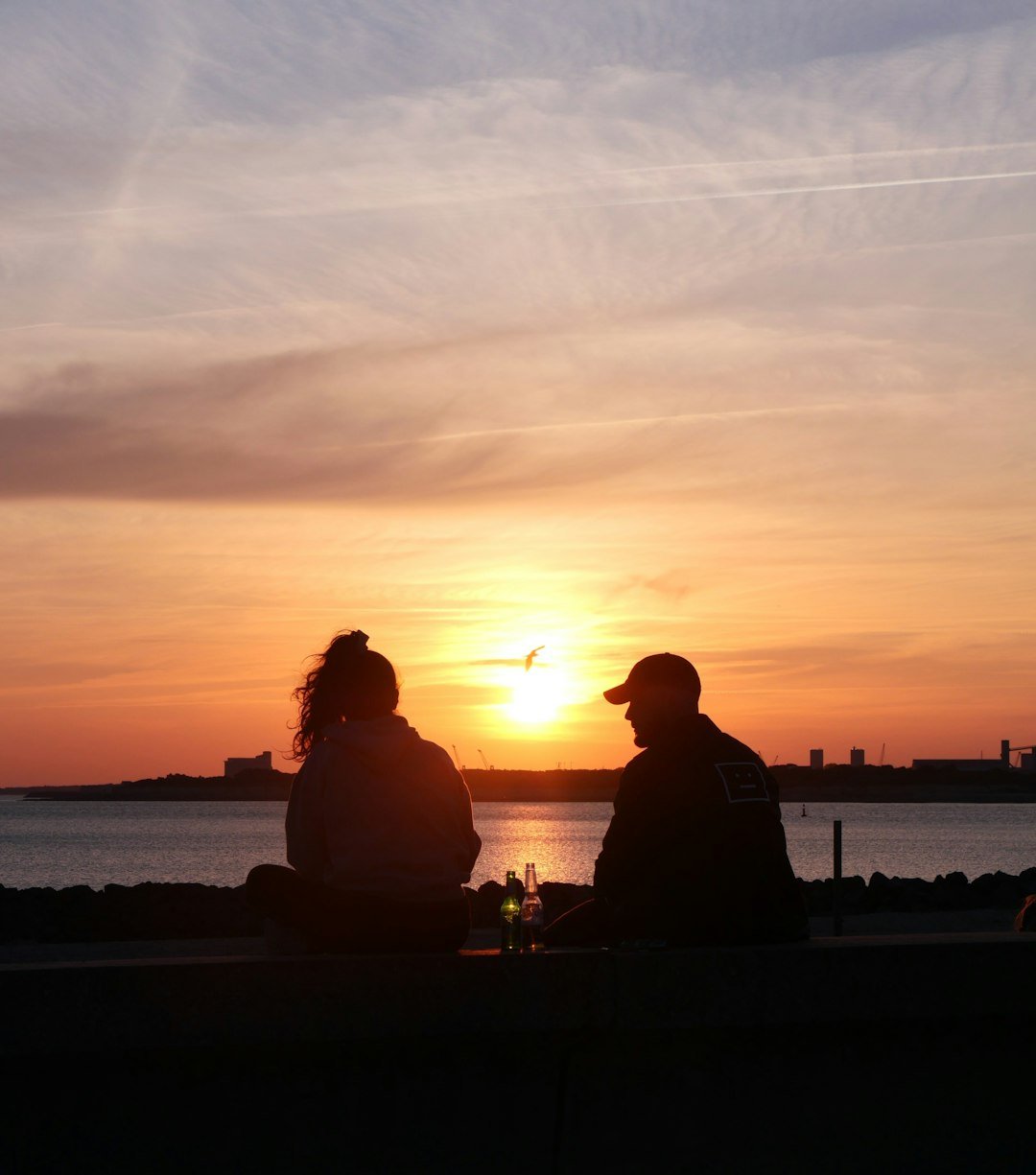 a couple of people sitting on a bench watching the sunset